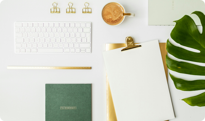 Arbeitsplatz mit weißer Tastatur, Notizblock und goldfarbenen Büroaccessoires auf hellem Schreibtisch